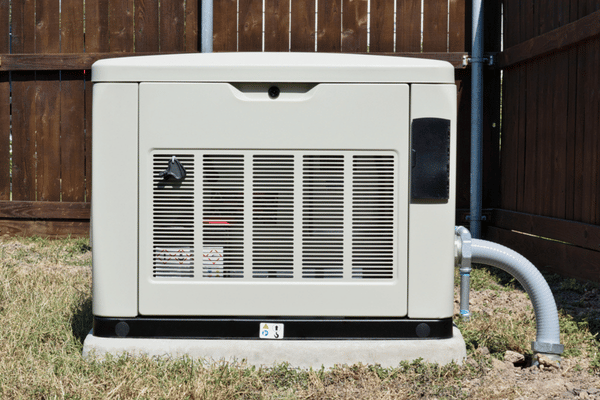 Standby generator sits on pad near fence after home generator installation for backup power
