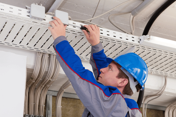 Technician installs wiring in ceiling tray during commercial electrical repair to restore safe circuits