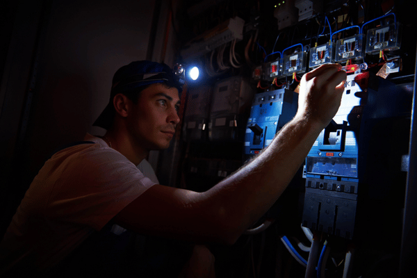 Technician inspects electrical panel with headlamp during outage while emergency electrician finds faulty wiring